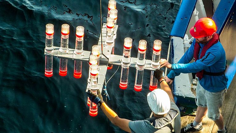 Two men lowering a research device from a research vessel into the water
